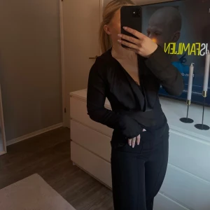 Svart blus  - Elegant svart blus med vattenfalls urringning och långa ärmar. Perfekt för en stilren look. Tröjan är i satin upptill och mesch ner mot magen.🥰