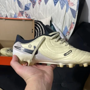 Beige fotbollsskor från Nike - Säljer ett par stilrena beige fotbollsskor från Nike med svarta detaljer och snörning. Perfekta för fotbollsplanen med en snygg design och bra grepp.