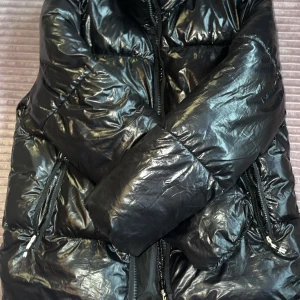 Svart pufferjacka från H&M - Säljer en svart pufferjacka från H&M. Jackan har en glansig yta och är utrustad med dragkedja framtill. Perfekt för kyligare dagar med sin vadderade design. Den har ej luva. Den är tyvärr för liten för mig så därför ingen bild när den sitter på, den värmer gott och håller kylan ute. Den är använd ca 5ggr och skicket är som nytt. Inga skador eller fläckar. Nytt pris vart cirka 250kr.