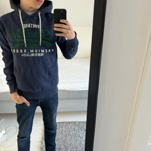 Mörkblå hoodie från Superdry - Säljer en snygg mörkblå hoodie från Superdry med grönt  tryck på framsidan. Den är perfekt för dagens stil. Den passar dig mellan 176-183 ish. Tycker den är sjukt snygg och det är bara att ställa frågor!
