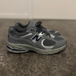 Grå och svarta sneakers från New Balance - Snygga och bekväma sneakers från New Balance i grått och svart. Skorna har en klassisk design med snörning och en robust sula för extra komfort. Perfekta för både vardag och träning.