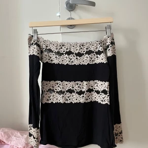 Svart offshoulder topp med spetsdetaljer - Säljer en elegant svart offshoulder topp från Intimissimi med vackra spetsdetaljer i vitt. Toppen har långa ärmar och en stilren design som passar perfekt för speciella tillfällen. Perfekt för dig som vill ha något unikt och stilrent i garderoben.
