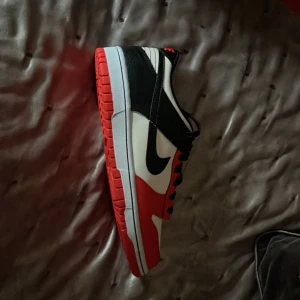 Nike Dunk Low Chicago  - Snygga Nike Dunk Low sneakers i en klassisk färgkombination av svart, vit och röd. Skorna har en röd sula och ikonisk Nike-logga på sidan. Perfekta för en stilren och sportig look. Skorna är helt oanvända aldrig använt dom, kom dm för pris och mer🙌🏻👍