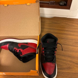 Nike Air Jordans i svart och rött - Snygga Nike Air Jordans i klassisk svart och röd färgkombination. Skorna har en hög design med snörning och den ikoniska swoosh-loggan på sidan. Perfekta för både stil och komfort.