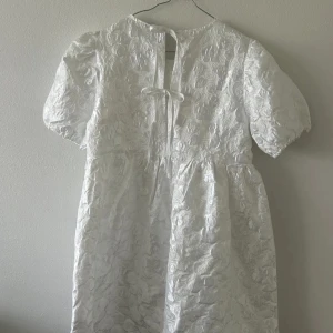 Vit blommig klänning med knyt - Vit klänning med blommigt mönster och korta puffärmar. Knytning i ryggen. Perfekt för studenten!!! S men passar absolut M och L