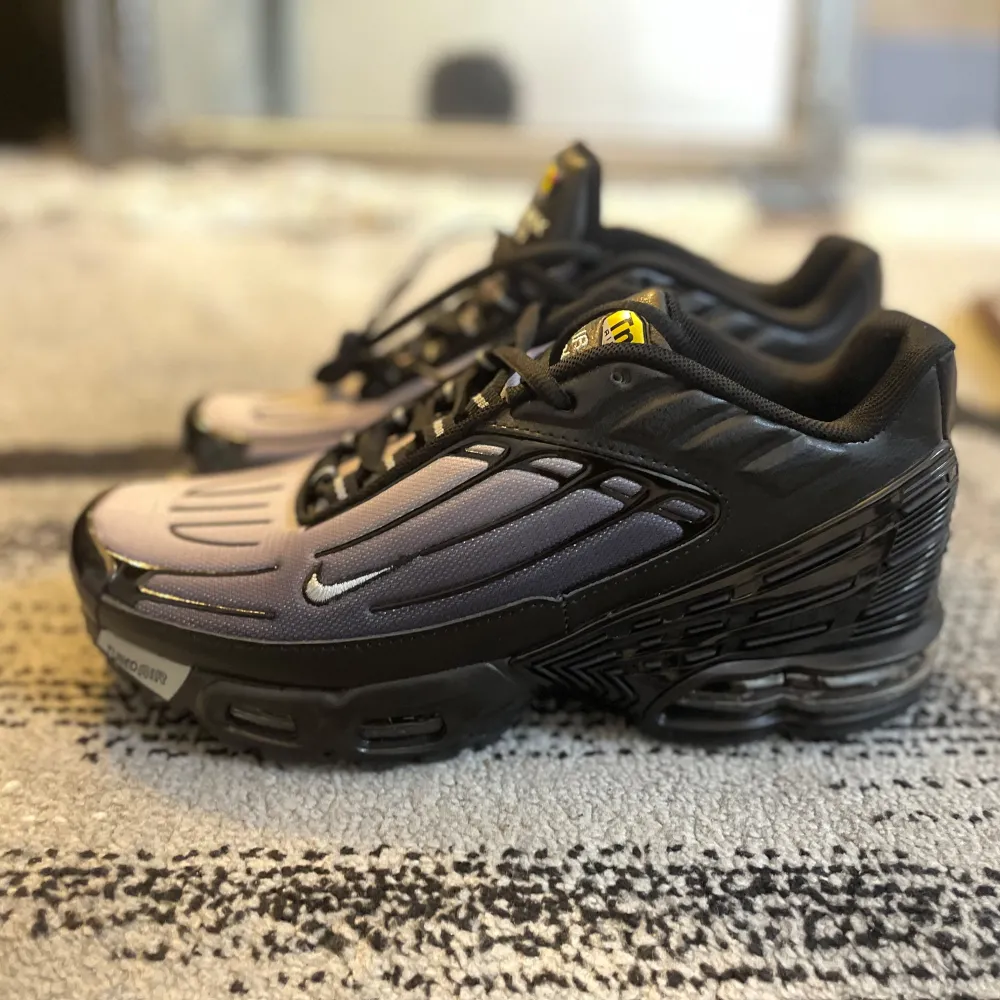 Snygga Nike Air Max Plus sneakers i en stilren svart och grå färgkombination. Skorna har en unik design med synlig Air Max-dämpning och TN-logga på tungan. Perfekta för både stil och komfort.. Kengät.