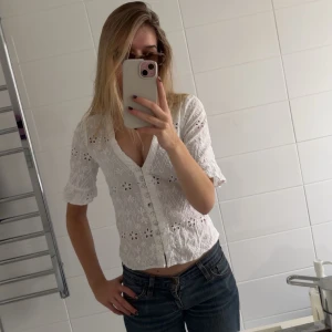 Vit blus från Pieces - Säljer en söt vit blus från Pieces med broderade blommor och knappar framtill. Blusen har en v-ringad design och trekvartsärmar, perfekt för vår och sommar💕