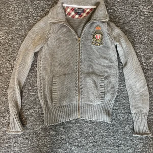 Grå stickad kofta från Ralph Lauren - Säljer en snygg grå stickad kofta från Ralph Lauren med dragkedja och broderad logga på bröstet. Slim fit, står M på tagen men sitter som XS/S. Materialet är en blend med bomull och kashmir. 