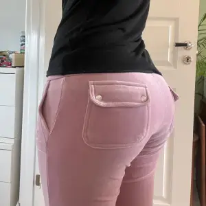 Säljer ett par rosa-lila mjukisbyxor från Juicy Couture med fickor som har knappdetaljer. Byxorna har en bekväm passform och är perfekta för en avslappnad stil. De är tillverkade i ett mjukt material som känns skönt mot huden. Denna färgen går inte att hitta längre på marknaden och fanns bara att köpa under en kort period viket gör dem väldigt unika och speciella då det bara finns i ett begränsat antal. Priset går att pruta.