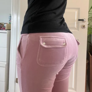 Rosa-lila Juicy byxor - Säljer ett par rosa-lila mjukisbyxor från Juicy Couture med fickor som har knappdetaljer. Byxorna har en bekväm passform och är perfekta för en avslappnad stil. De är tillverkade i ett mjukt material som känns skönt mot huden. Denna färgen går inte att hitta längre på marknaden och fanns bara att köpa under en kort period viket gör dem väldigt unika och speciella då det bara finns i ett begränsat antal. Priset går att pruta.