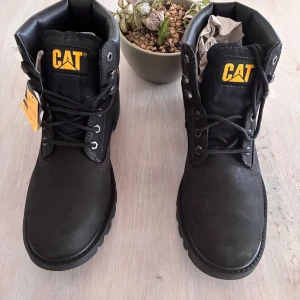 Svarta boots från Caterpillar - Säljer ett par robusta svarta boots från Caterpillar med snörning och märkets logga i gult. Skorna har en slitstark sula och är perfekta för utomhusaktiviteter. Tillverkade i syntetmaterial med en bekväm passform.