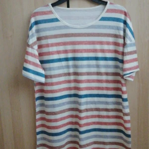 Randig t-shirt i polyester - Säljer en randig t-shirt i mjukt och stretchigt material. T-shirten har ränder i blått, rött och beige på en vit bas. Perfekt för en avslappnad stil.