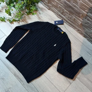 Svart stickad tröja från Ralph Lauren - Säljer en stilren svart stickad tröja från Polo Ralph Lauren med det klassiska logotypbroderiet på bröstet. Tröjan har en rund halsringning och långa ärmar med ribbade muddar. Perfekt för en elegant och avslappnad look. Passar bäst M‼️‼️