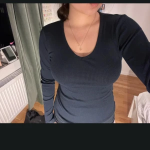 Mörkblå ribbad långärmad tröja med v-ringning - Säljer en mörkblå långärmad tröja med v-ringning. Tröjan är ribbad och har en tight passform som framhäver figuren. Perfekt att styla med jeans eller kjol för en enkel och snygg look.