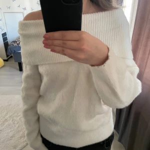 Vit offshoulder stickad tröja - Säljer en vit stickad tröja med offshoulder-krage. Tröjan har lång ärm och är mjuk och skön, perfekt för kyligare dagar. Snygg och enkel att matcha med olika outfits.