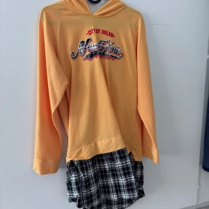 Gul hoodie med tryck från New York - Säljer en gul hoodie med tryck 'City of Dream - New York' på bröstet. Tröjan har långa ärmar och huva, perfekt för en avslappnad stil. Mjuk och skön, passar till många tillfällen.