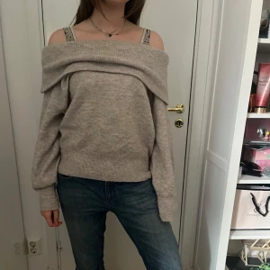 Beige offshoulder stickad tröja - Säljer en beige stickad offshoulder-tröja med bred krage. Tröjan har lång ärm och en avslappnad passform, perfekt för lager-på-lager. Supermjuk och skön att bära till jeans eller kjol.
