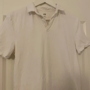 Vit piké t-shirt från H&M - Vit piké t-shirt från H&M med klassisk krage och knappar framtill. Kortärmad och i enkel, stilren design. Perfekt för en clean och avslappnad look.