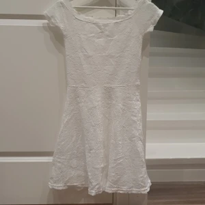Vit spetsklänning med kort ärm - Söt vit klänning i spets med korta ärmar och rundad halsringning. Klänningen har en lätt utställd kjol och är helfodrad. Perfekt för somriga tillfällen eller studentfirande. Materialet är mjukt och följsamt.