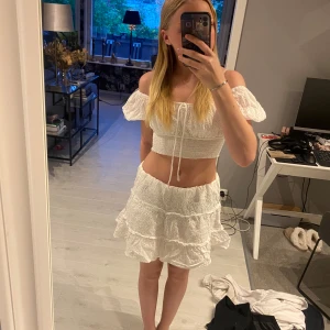 Vit tvådelad klänning med volanger - Säljer en söt vit tvådelad klänning med kort ärm och volangdetaljer. Båda delarna är i storlek xs. Toppen har knyt framtill och kjolen är medel kort med flera lager volanger. Båda delarna är från en butik i Italien.  