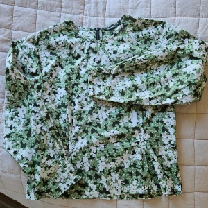 Blommig långärmad blus från Marimekko - Säljer en blommig långärmad blus från Marimekko i grönt, vitt och inslag av rosa och gult. Blusen är i 100% bomull och har dragkedja bak. Perfekt för dig som gillar färg och mönster!