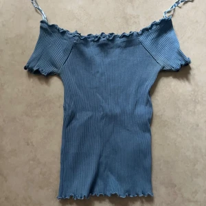 Blå ribbad topp från Blue Seven - Säljer en ljusblå ribbad topp från Blue Seven med offshoulder och volangkant upptill och nedtill. Toppen har korta ärmar och smala axelband.  Perfekt för dig som gillar en söt och enkel stil! 