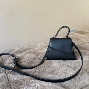 Svart mini axelväska från Gina Tricot - Säljer en svart mini axelväska från Gina Tricot med stilren design och justerbar axelrem. Knappt använt