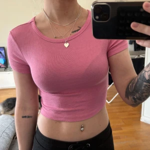 Rosa croppad ribbad t-shirt - Säljer en rosa croppad t-shirt med tight passform. Toppen är ribbad och har korta ärmar samt rund halsringning. Perfekt för en trendig och avslappnad stil.