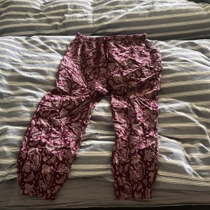 Vinröda paisleymönstrade byxor från ISABELLA - Paisleymönstrade vinröda byxor från ISABELLA i storlek M (40/42). Byxorna har resår i midjan och snörning framtill för extra komfort. Perfekta för en avslappnad stil med sitt mjuka bomullsmaterial.