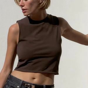 Brun croppad ärmlös topp - Säljer en brun croppad topp med hög hals och ärmlös design. Perfekt för varma dagar och enkel att matcha med jeans eller kjol. Stilren och modern look.
