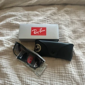 Svarta solglasögon från Ray-Ban - Säljer ett par klassiska svarta solglasögon från Ray-Ban med rektangulär form. Kommer med originalfodral och förpackning. Perfekta för soliga dagar och en tidlös accessoar till din stil. Helt oanvända!!