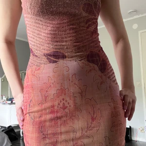 Rosa mönstrad tight klänning - Säljer en tight klänning i rosa och lila toner med blommigt mönster. Klänningen är ärmlös och har en kroppsnära passform, perfekt för dig som gillar färg och mönster. Materialet känns mjukt och följsamt.