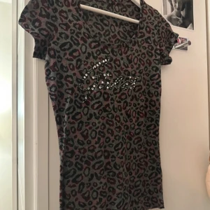 Guess storlek S mer som XS - Säljer en leopardmönstrad t-shirt från Guess med glittrande strassdetaljer på bröstet. T-shirten har korta ärmar och en figurnära passform. Perfekt för dig som vill sticka ut med en cool och trendig look. Mer som storlek xs