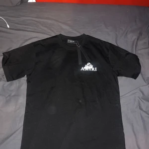 Svart t-shirt med ängeltryck från Amiri - Säljer en svart t-shirt från Amiri med vit logga och ängeltryck både fram och bak. T-shirten har rund halsringning och normal passform. Perfekt för dig som gillar streetwear och exklusiva märken.