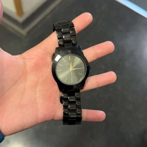 Svart armbandsur med metallänk - Stilren svart klocka från MVMT med svart metallänk och rund urtavla. Urtavlan har guldiga visare och markeringar vilket ger en snygg kontrast mot det svarta. Perfekt accessoar för dig som gillar minimalistisk design.