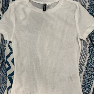 Vit t-shirt från H&M Divided - Klassisk vit t-shirt från H&M Divided. Enkel och stilren design med rund halsringning och korta ärmar. Lite genomskinlig men ett perfekt basplagg! Använt 1 gång, strl S. 70kr