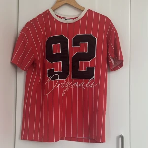 Röd randig t-shirt med tryck från FB Sister - Röd t-shirt från New Yorker med vita vertikala ränder och stort svart tryck '92' framtill. Vit ribbad krage som kontrast. Perfekt för en sportig och avslappnad stil. Den är i storlek XS men forfarande stretchig och ”stor” i modellen, finns också lite fläckar runt halsen men inget som lägga märke på 