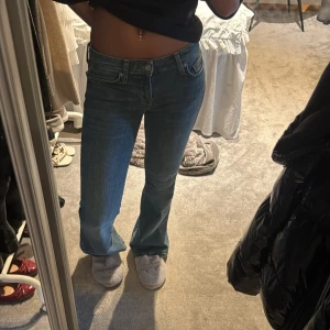 Blå utsvängda jeans med låg midja - Säljer mina blåa jeans med låg midja. Jeansen har fem fickor och stängs med dragkedja och knapp. Perfekta till vardags för en avslappnad stil.