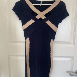 Svart och beige klänning från Chiara Forti Milano - Snygg svart kortklänning med beigea detaljer från Chiara Forti Milano. Klänningen har korta ärmar och ett unikt korsat mönster framtill som ger en cool look. Figurnära passform och stretchigt material som framhäver siluetten.