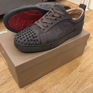 Christian Louboutins - Säljer ett par gråa sneakers från Christian Louboutin med mattsvarta nitar på tån och klassisk röd sula. Skorna har snörning och är tillverkade i mocka med gråa detaljer. Perfekta för dig som vill sticka ut med en lyxig touch. Pris går att diskuteras. Säljs pga har tröttnat lite på dem så ska köpa nya skor. Riktigt goa skor👌💪💯