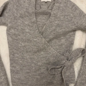 Grå omlottstickad tröja från Gina Tricot - Säljer grå stickad omlott-tröja från Gina Tricot i ullblandning. Tröjan är nästintill oanvänd endast använd en gång! Super fin! 