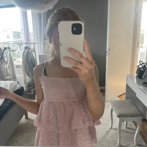 Ljusrosa volangtopp - Säljer en ljusrosa topp med volanger och smockat tyg. Toppen är ärmlös och har en luftig, flowy passform som passar perfekt till sommaren. Supersöt och enkel att matcha med olika outfits!