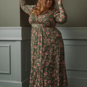 Linda Marie kollektion för Ellos  - Säljer en grön långklänning med rosa och gula blommor. Klänningen har lång ärm och markerad midja med knytning för en smickrande siluett. Perfekt för vår och sommar!