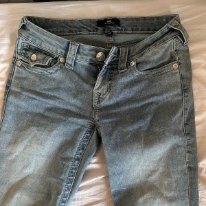 Ljusblå bootcut jeans från True Religion - Säljer ett par ljusblå jeans från True Religion, modell Joey Low Rise Flare i storlek w25. Jeansen har en väldigt låg midja, utsvängda ben och klassiska detaljer med silverfärgade knappar och broderade bakfickor. Jag säljer de för att de är för långa för mig. Har använt de några enstaka gånger och kan möjligtvis vara lite slitna längst ner på fötterna men inte alls mycket. 💕