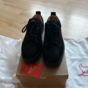 Svarta sneakers från Christian Louboutin - Säljer ett par svarta sneakers från Christian Louboutin med klassisk röd sula. Skorna har snörning och är tillverkade i mocka med svarta detaljer. Perfekta för dig som vill ha något exklusivt och stilrent. 