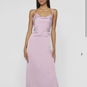 Ljuslila långklänning med smala axelband - Säljer en elegant ljuslila långklänning med smala axelband och lätt v-ringad halsringning. Klänningen har en slät, figurnära passform och är tillverkad i ett glansigt material som ger en lyxig känsla. Perfekt för sommarens speciella tillfällen.