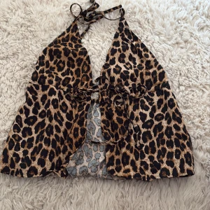 Leopardmönstrad croppad halterneck-top - Säljer en croppad halterneck-top med leopardmönster och knytning i ryggen. Toppen har en djup v-ringning och är ärmlös, perfekt för att sticka ut med en trendig look.