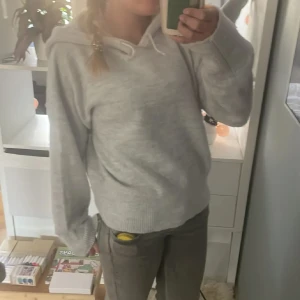 Ljusgrå stickad hoodie från Gina Tricot - Mysig ljusgrå stickad hoodie från Gina Tricot med huva och långa ärmar. Tröjan har ribbade muddar vid ärmslut och nederkant, perfekt för en avslappnad och stilren look. Säljer 2 av exakt samma💕