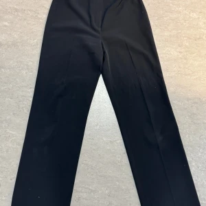 Svarta kostymbyxor från H&M - Klassiska svarta kostymbyxor från H&M i rak modell. Byxorna har hög midja och raka ben, perfekta för en stilren look. Passar till många olika tillfällen och är lätta att matcha med olika toppar. Öppen för bud!💕