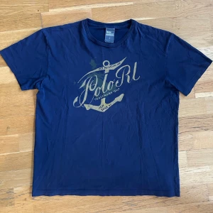 Polo Ralph Lauren tshirt  - Säljer en mörkblå t-shirt från Polo RL med ett stort tryck på framsidan. T-shirten har en klassisk rund hals och korta ärmar.